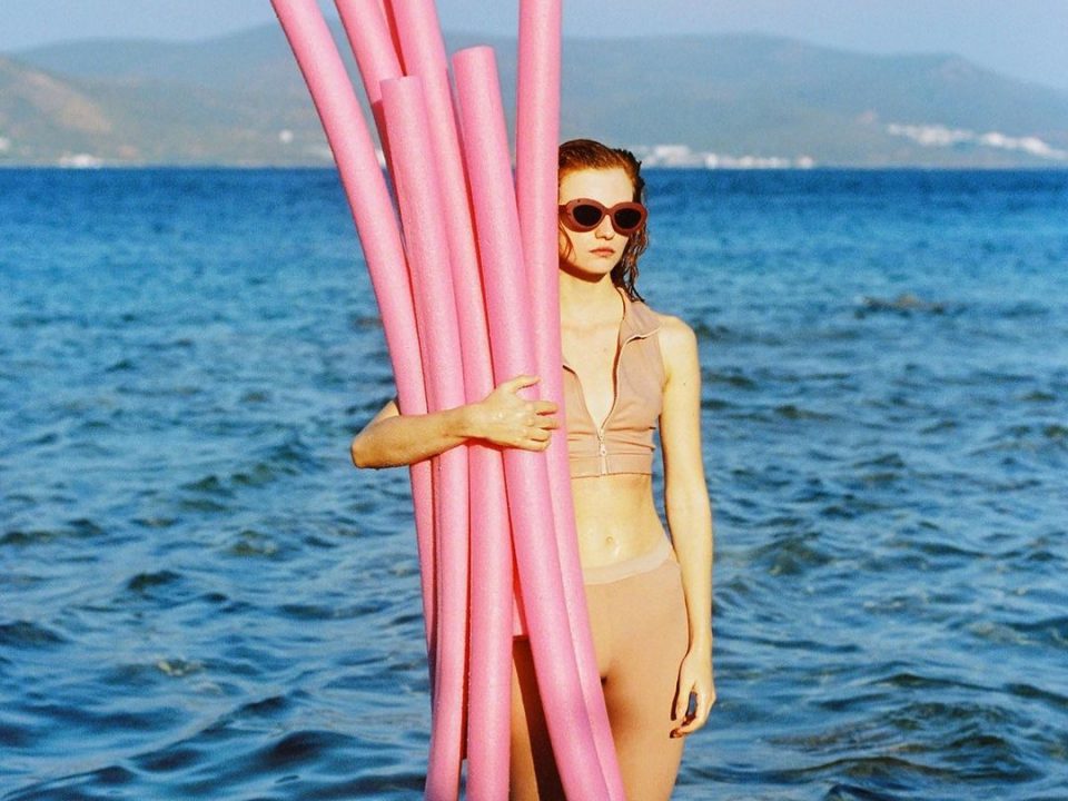 Woman holding pink plastic tubes in the ocean.